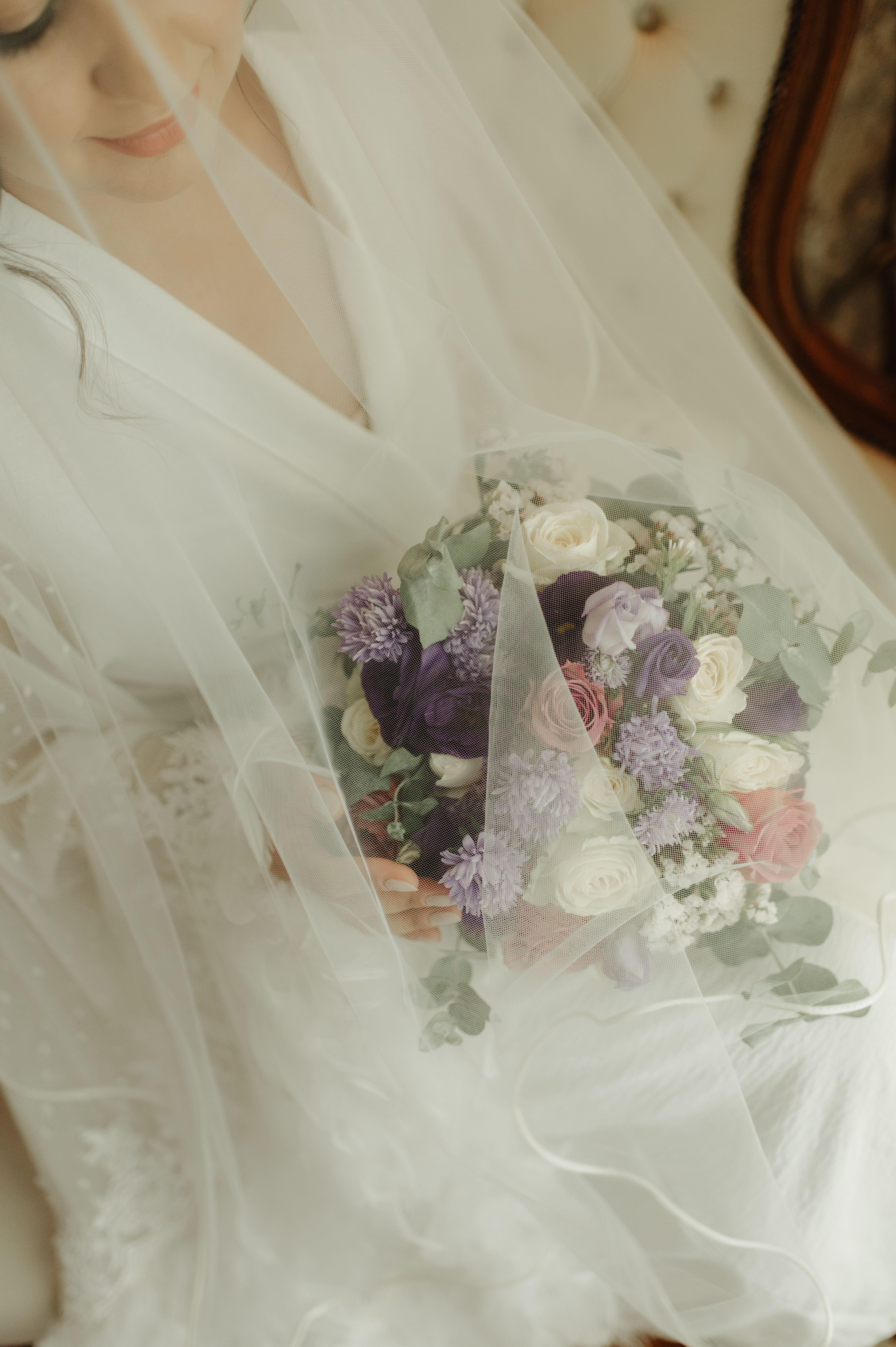 Noiva com véu segurando buquê de flores em tons de roxo e rosa